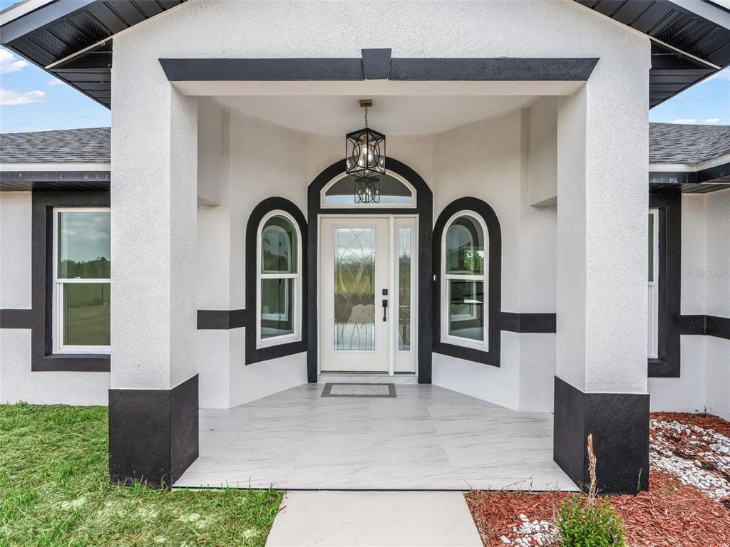 The exterior entryway features a white stucco facade with black trim, arched windows, and tile — 14461 SE 80TH STREET, MORRISTON, FL