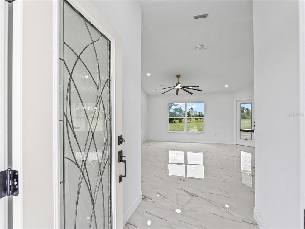 A view from a glass-paneled front door into a bright living area with marble flooring — 14461 SE 80TH STREET, MORRISTON, FL