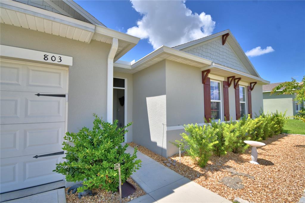 A beige single-story house exterior features a white garage door, brown shutters, and landscaping — 803 AUBURN GROVE COURT, AUBURNDALE, FL