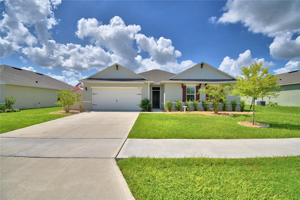 A single-story suburban house features a two-car garage, light-colored stucco siding, and a green lawn — 803 AUBURN GROVE COURT, AUBURNDALE, FL