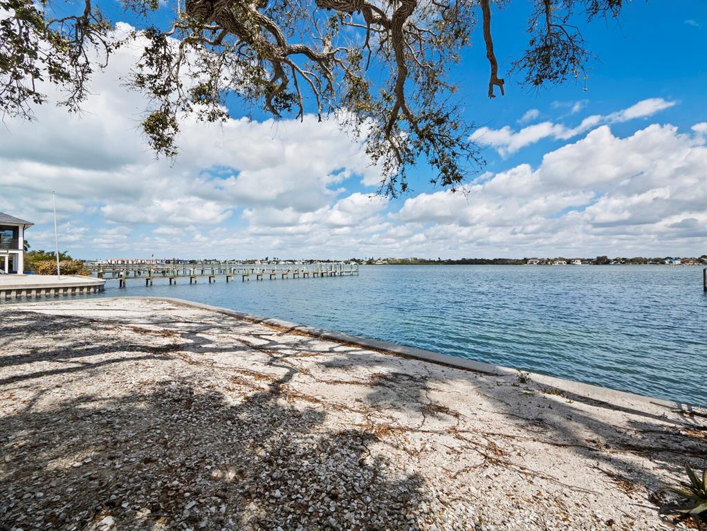 A shell-covered shoreline overlooks a calm bay with a long wooden pier under blue skies — 1267 STARBOARD LANE, SARASOTA, FL