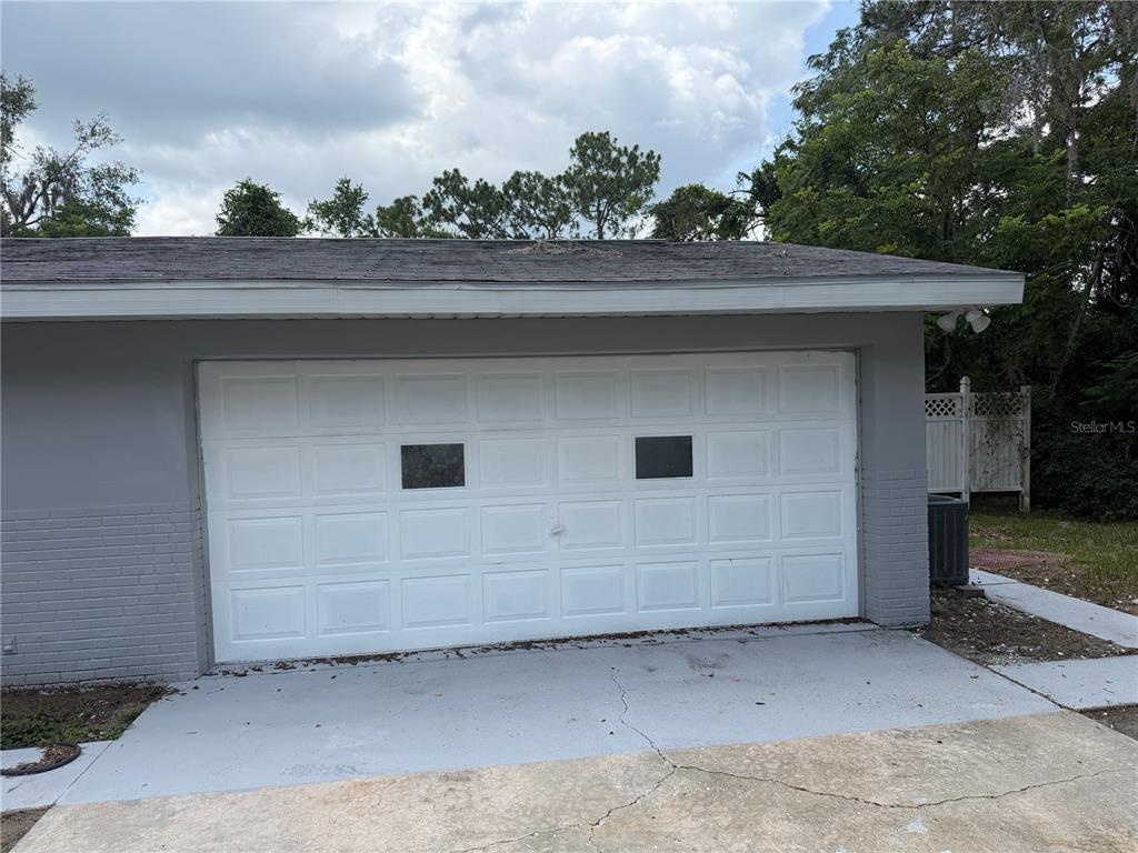 A gray exterior wall features a white two-car garage door with two rectangular windows — 1405 EDEN DRIVE, INVERNESS, FL