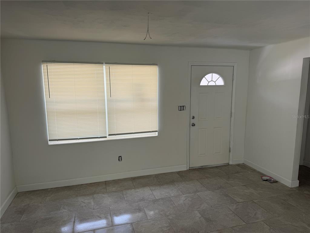 A room with white walls, tiled floors, a window with blinds, and an entry door — 1405 EDEN DRIVE, INVERNESS, FL