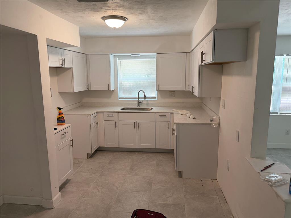 A kitchen with white cabinets, light countertops, a sink under a window, and tiled flooring — 1405 EDEN DRIVE, INVERNESS, FL