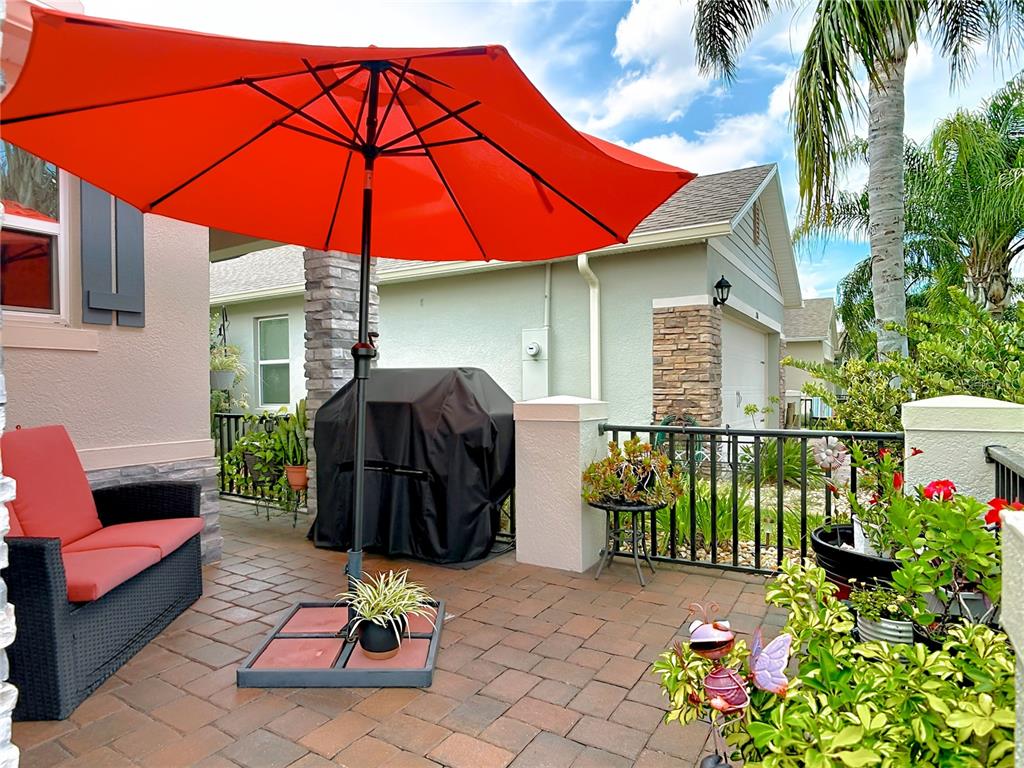A patio features a red umbrella, a covered grill, and a wicker sofa on pavers — 204 CARYOTA COURT, NEW SMYRNA BEACH, FL