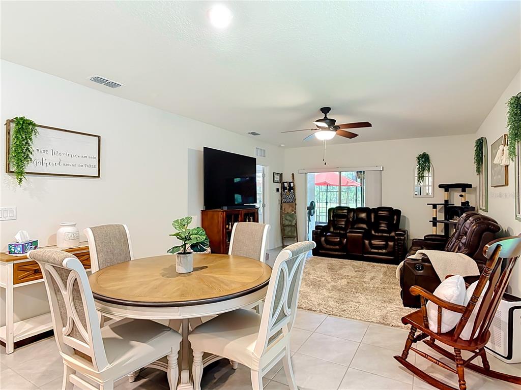 A dining area with a round table opens into a living room with tile flooring — 204 CARYOTA COURT, NEW SMYRNA BEACH, FL