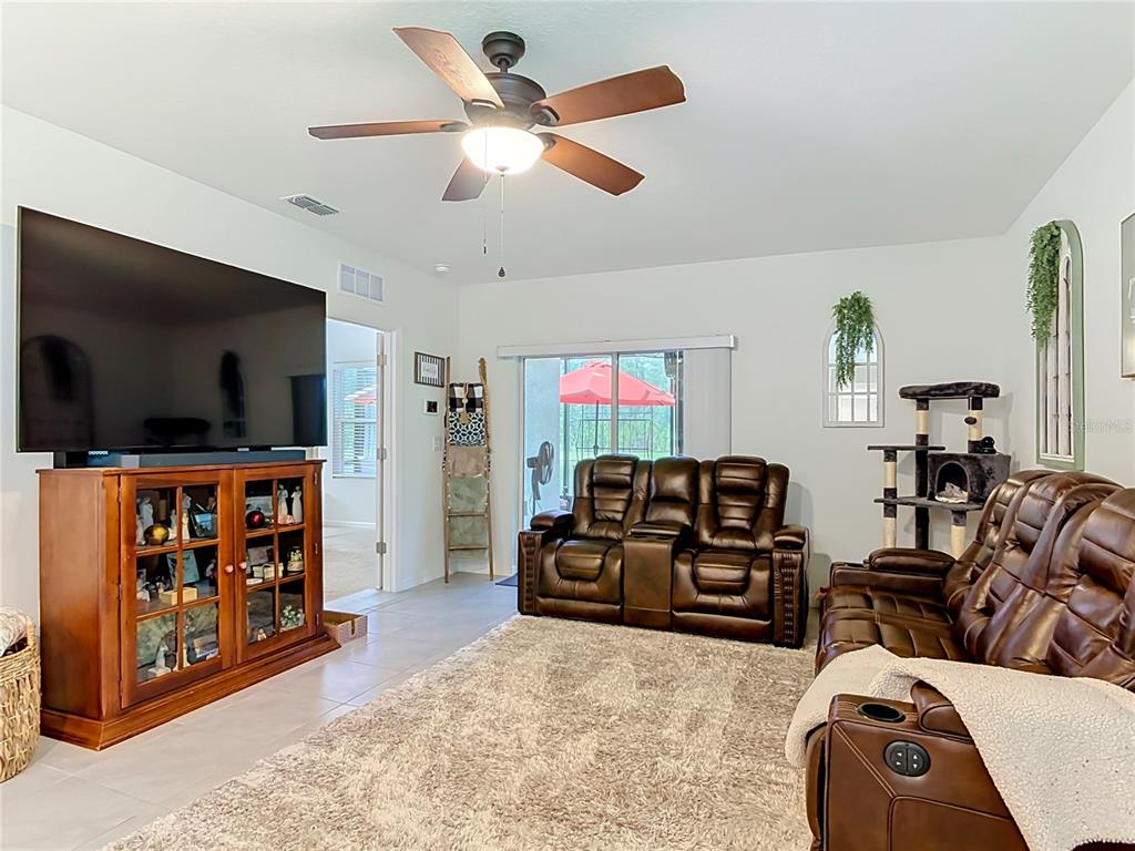 A living room features brown leather reclining furniture, a large television, and a ceiling fan — 204 CARYOTA COURT, NEW SMYRNA BEACH, FL