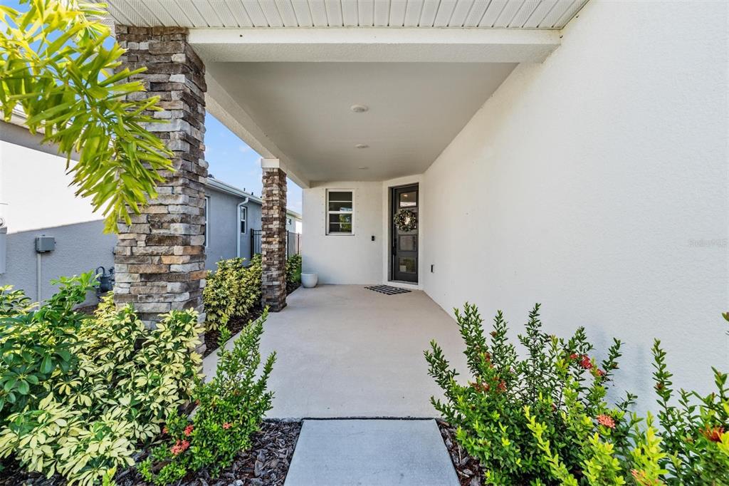 A covered front porch features stone-clad columns, a concrete floor, and a glass-paneled front door — 6276 GOLDEN BEACH DRIVE, APOLLO BEACH, FL