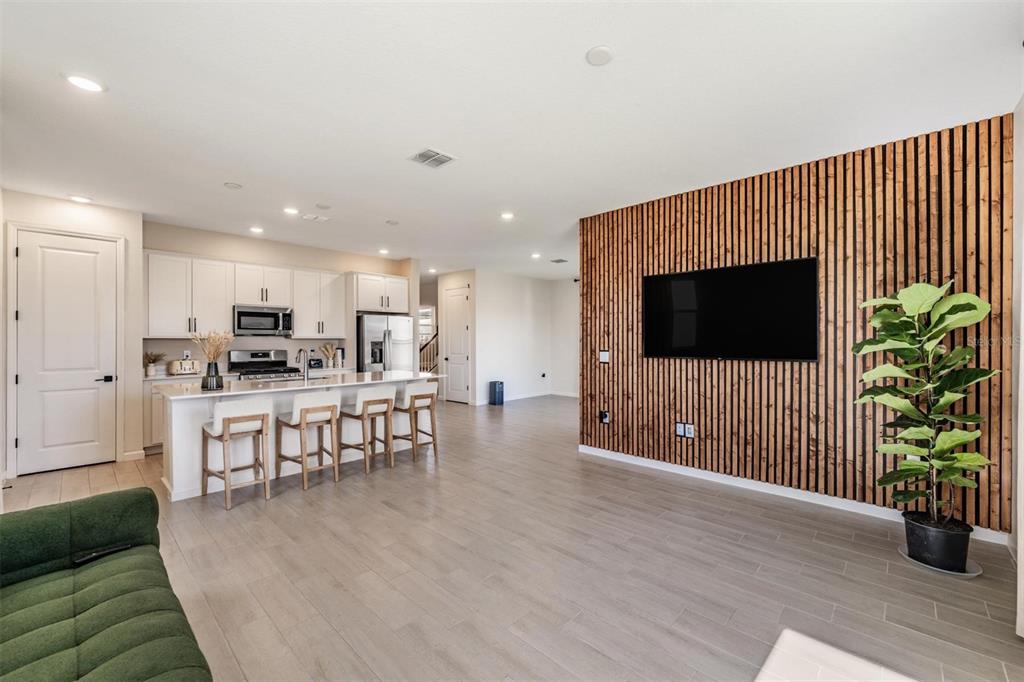 An open-concept living room features a wood-slat accent wall with a television and a kitchen — 6276 GOLDEN BEACH DRIVE, APOLLO BEACH, FL