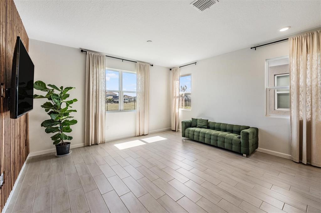 A living room features light wood-look tile floors, a green tufted sofa, and a television — 6276 GOLDEN BEACH DRIVE, APOLLO BEACH, FL
