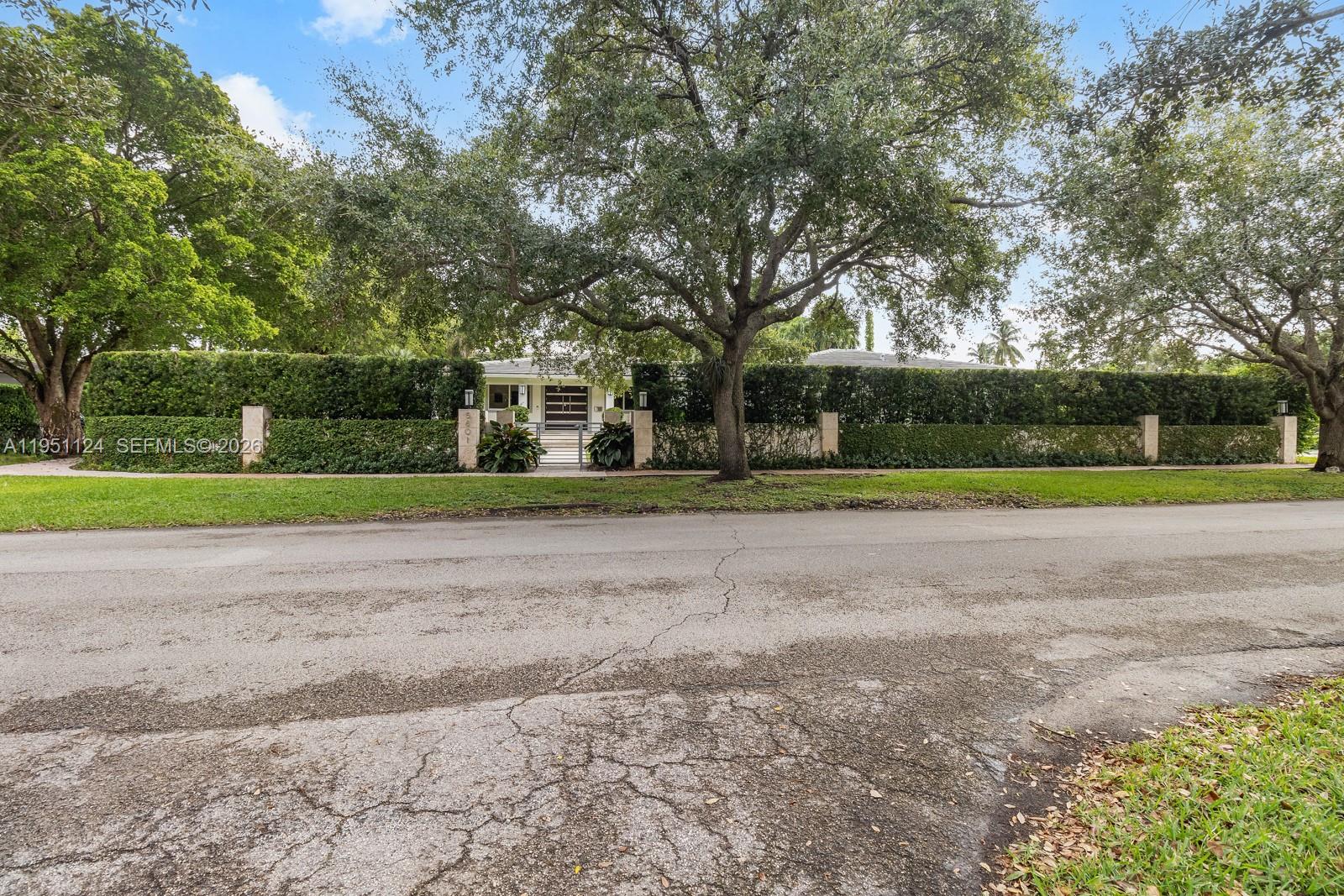 A gated house with a tall hedge and large trees sits behind a paved street — 5601 Maggiore St, Coral Gables FL 33146, CORAL GABLES, FL