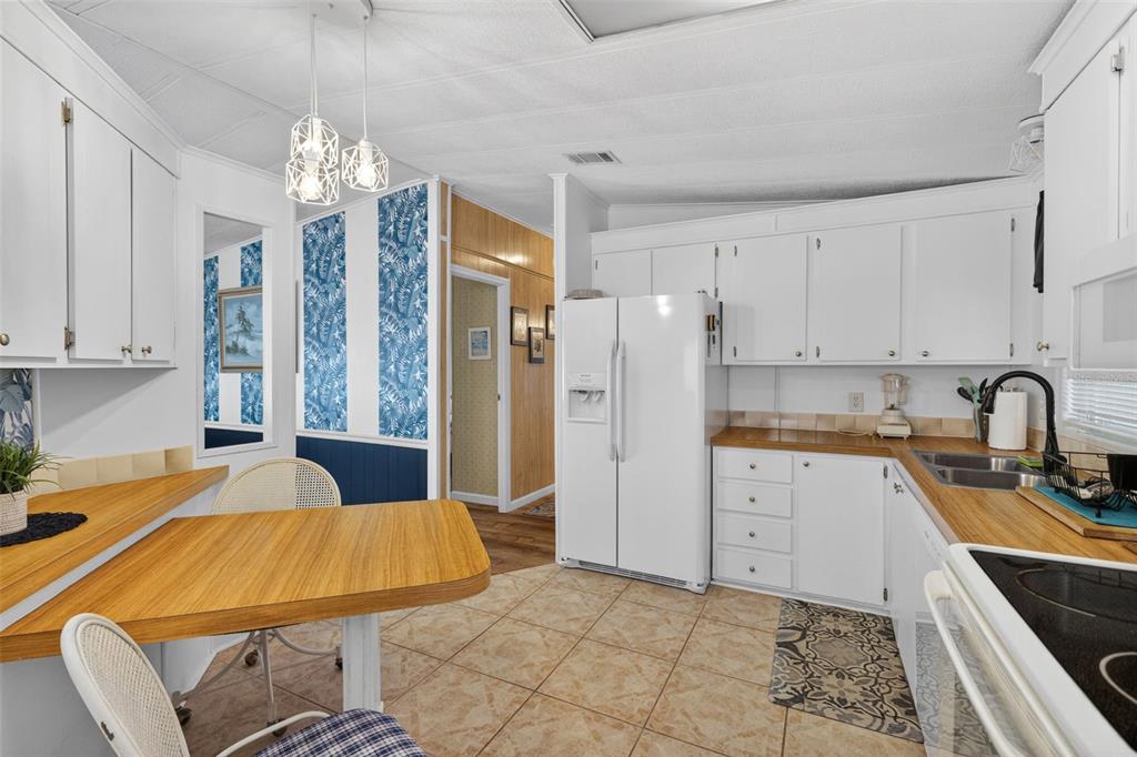 A kitchen features white cabinets, wood countertops, a white refrigerator, and a small dining area — 485 LOMA LINDA, NORTH PORT, FL