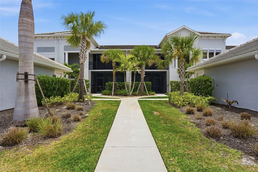 A concrete walkway leads to the entrance of a two-story residential building with palm trees — 14184 HERITAGE LANDING BOULEVARD UNIT 525, PUNTA GORDA, FL