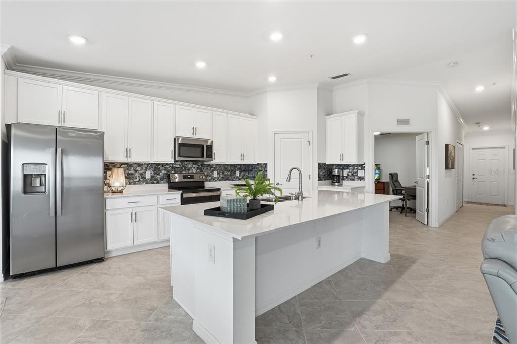 A modern kitchen features white cabinetry, stainless steel appliances, a large island, and tile flooring — 14184 HERITAGE LANDING BOULEVARD UNIT 525, PUNTA GORDA, FL