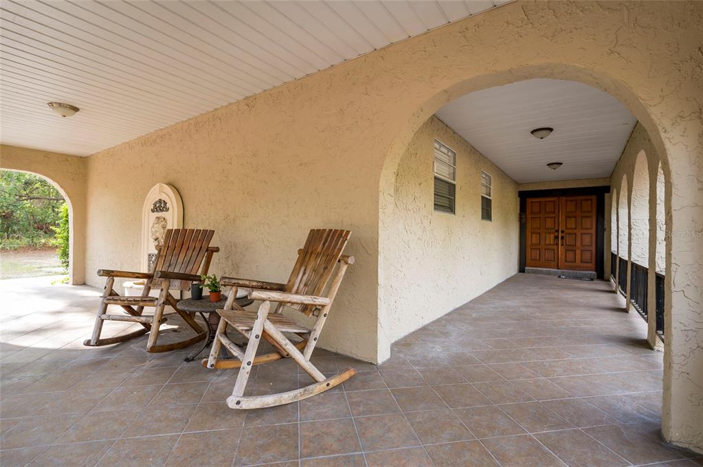 A covered porch features tile flooring, arched openings, and two wooden rocking chairs — 12311 OAKWOOD DRIVE, HUDSON, FL
