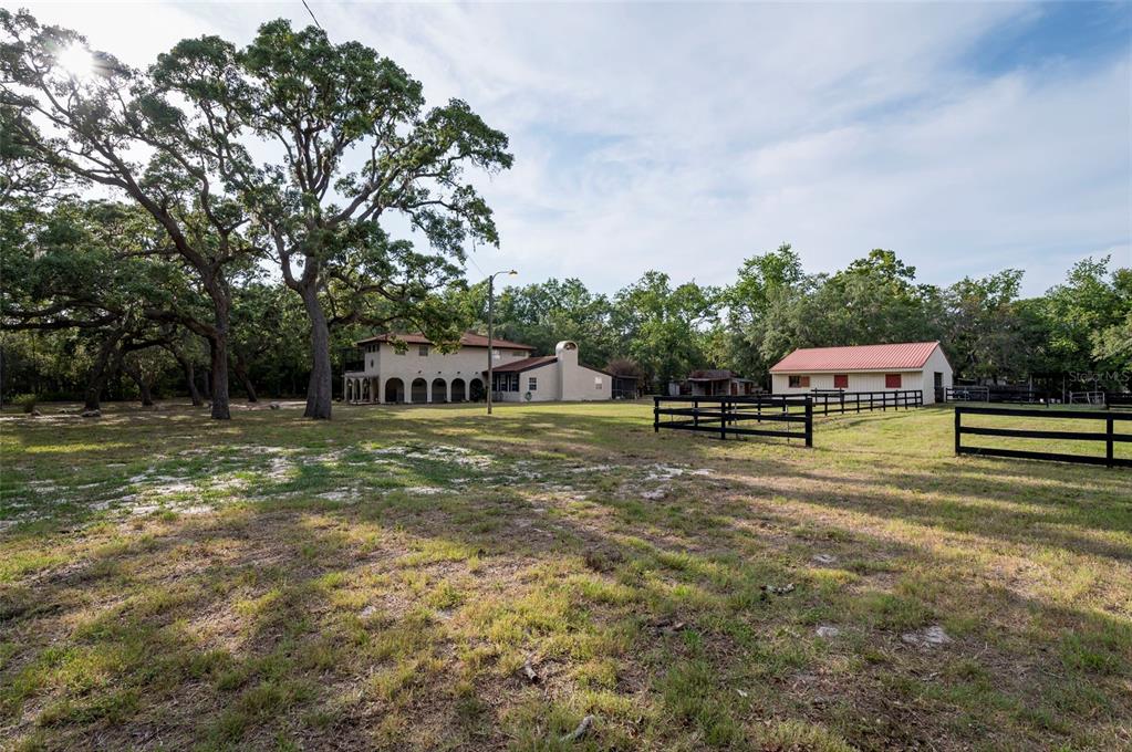 A two-story house and a separate barn sit on a grassy lot with large trees — 12311 OAKWOOD DRIVE, HUDSON, FL