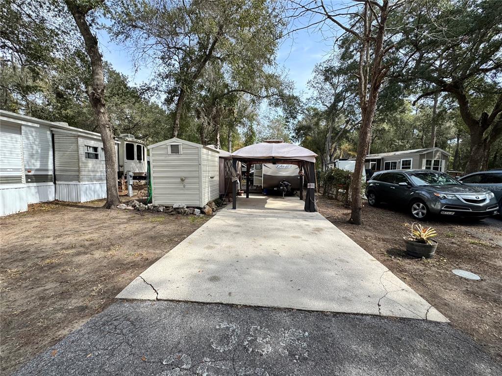 A concrete driveway leads to a covered patio, a storage shed, and parked recreational vehicles — 25325 NE 141ST STREET, SALT SPRINGS, FL