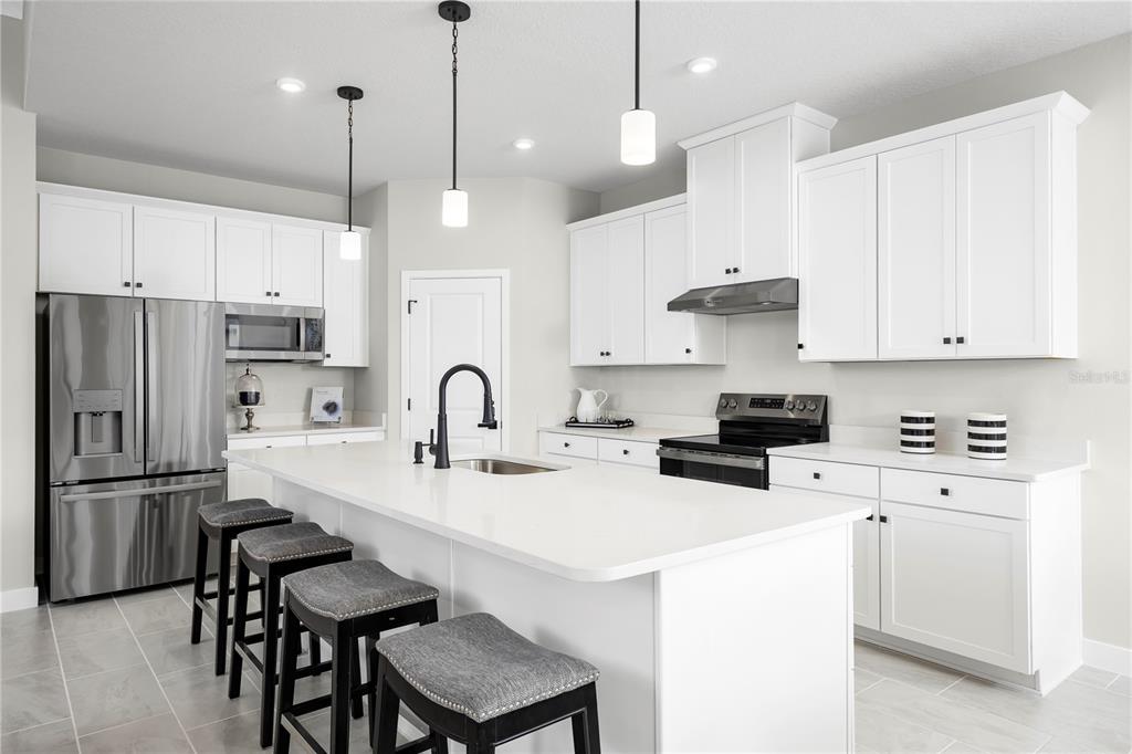 A modern kitchen features white cabinetry, a large central island with bar stools, and stainless appliances — 22174 PINE GROVE LOOP, LEESBURG, FL
