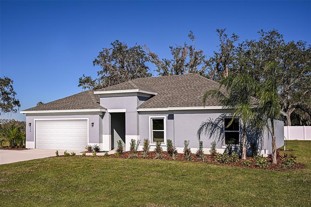 A single-story gray house with a two-car garage and a front entrance under a portico — 704 OAK HAMMOCK WAY, AVON PARK, FL