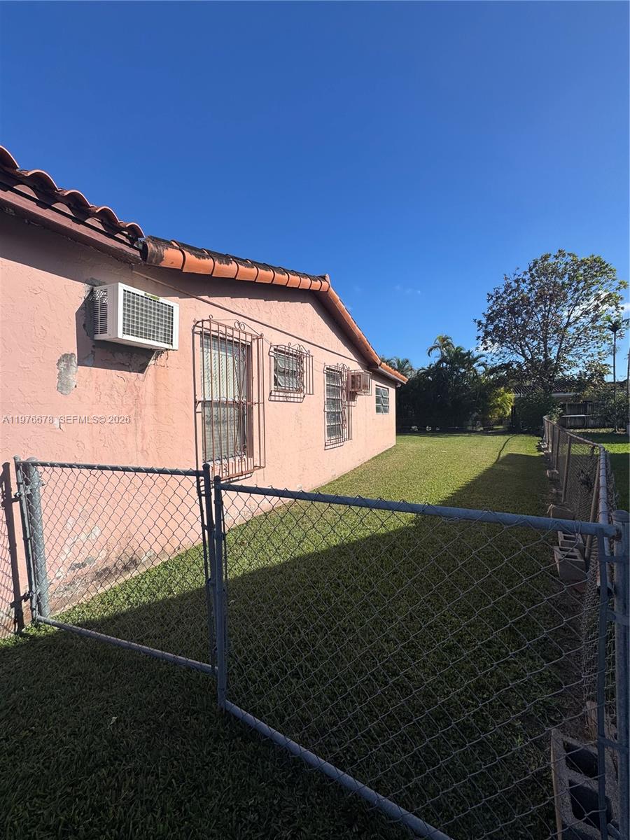 The exterior of a pink house features a chain-link fence and several window air conditioners — 10730 SW 66th Dr, Miami FL 33173, MIAMI, FL