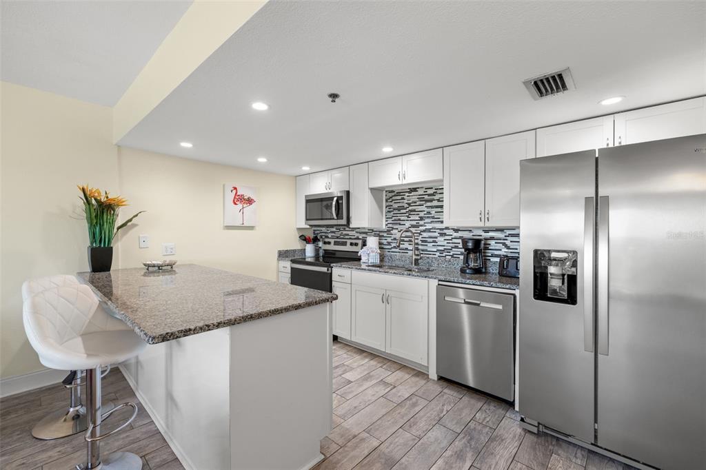 A modern kitchen features white cabinets, granite countertops, stainless steel appliances, and a breakfast bar — 18610 GULF BOULEVARD UNIT 709, INDIAN SHORES, FL