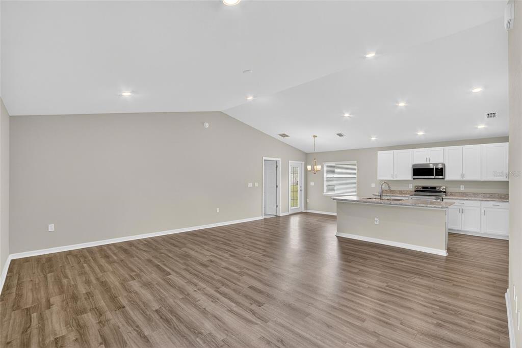 An open-concept living area features wood-look flooring, vaulted ceilings, and a kitchen with white cabinets — 1047 ARUBA AVENUE, MULBERRY, FL
