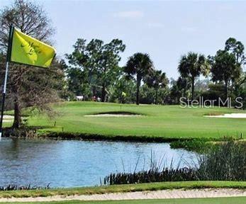 A golf course green sits behind a pond with a yellow flag in the foreground — 16061 GALENA AVENUE, PORT CHARLOTTE, FL
