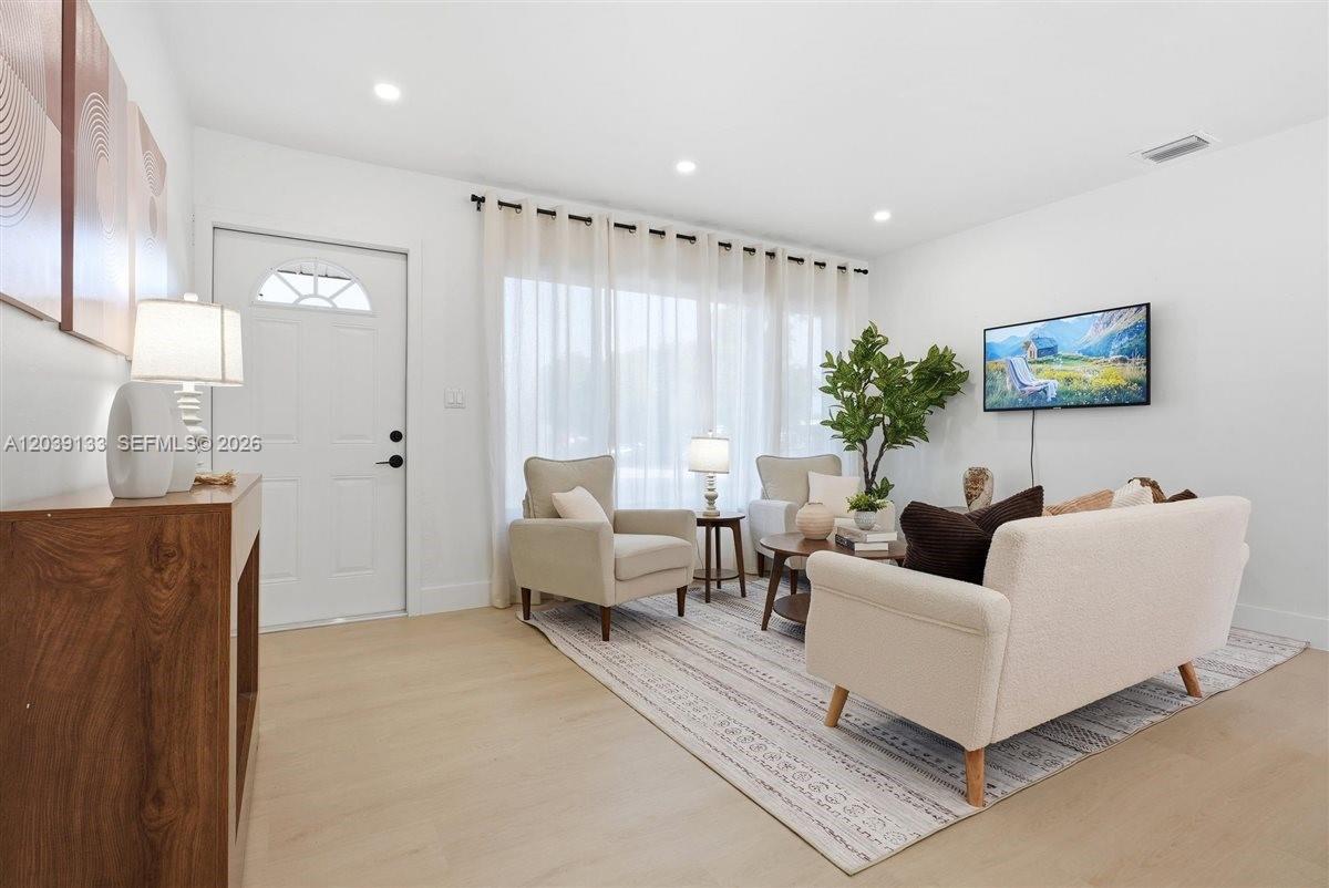 A bright living room features light wood flooring, a white sofa, and two armchairs — 4410 NE 3rd Ave, Deerfield Beach FL 33064, DEERFIELD BEACH, FL