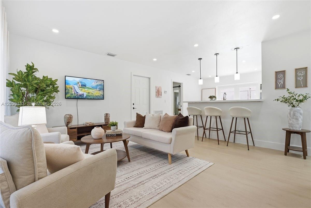 A bright living room features light wood floors, a neutral sofa, and a kitchen bar — 4410 NE 3rd Ave, Deerfield Beach FL 33064, DEERFIELD BEACH, FL