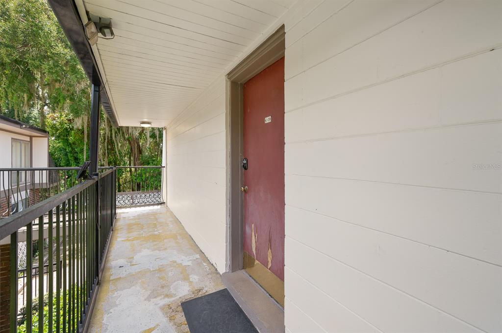 An exterior balcony features a red door, a black metal railing, and a concrete floor — 1700 SW 16TH COURT UNIT L26, GAINESVILLE, FL