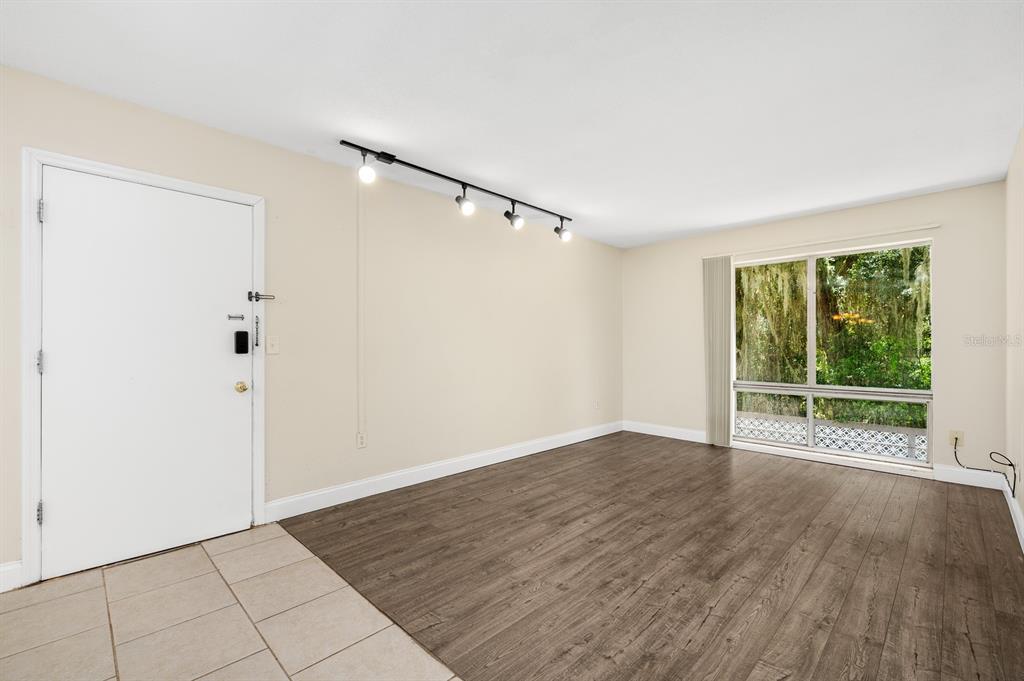 An empty room features light-colored walls, wood-look flooring, a track light, and a large window — 1700 SW 16TH COURT UNIT L26, GAINESVILLE, FL