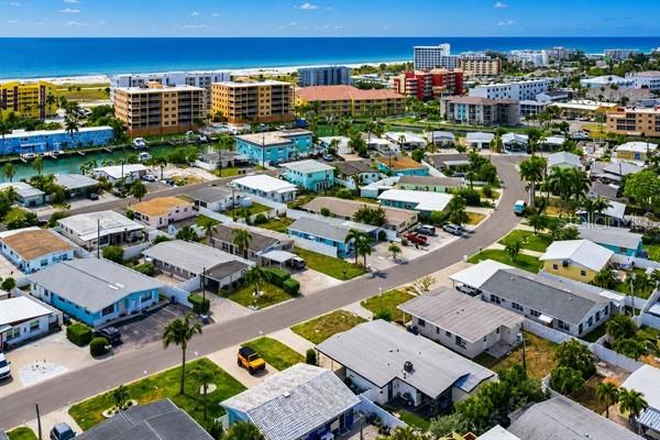 An aerial view shows a coastal neighborhood with houses, apartment buildings, and a nearby beach — 11355 2ND STREET E, TREASURE ISLAND, FL