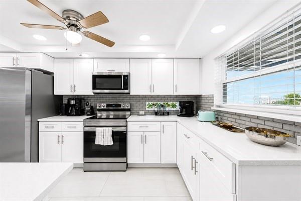 A modern kitchen features white cabinets, stainless steel appliances, and a gray subway tile backsplash — 11355 2ND STREET E, TREASURE ISLAND, FL