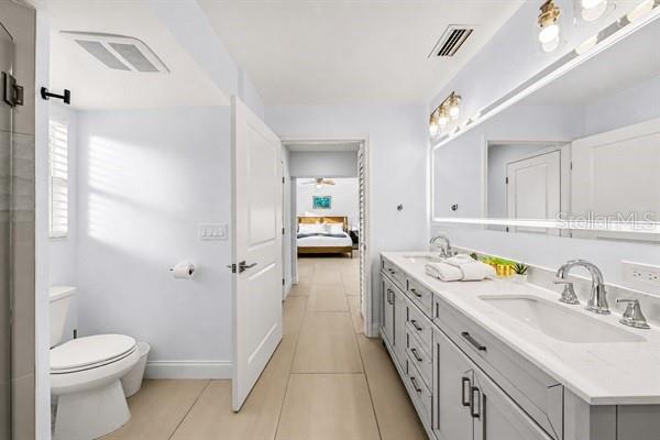 A bathroom with a double vanity, light gray cabinets, and a toilet, leading to a bedroom — 11355 2ND STREET E, TREASURE ISLAND, FL