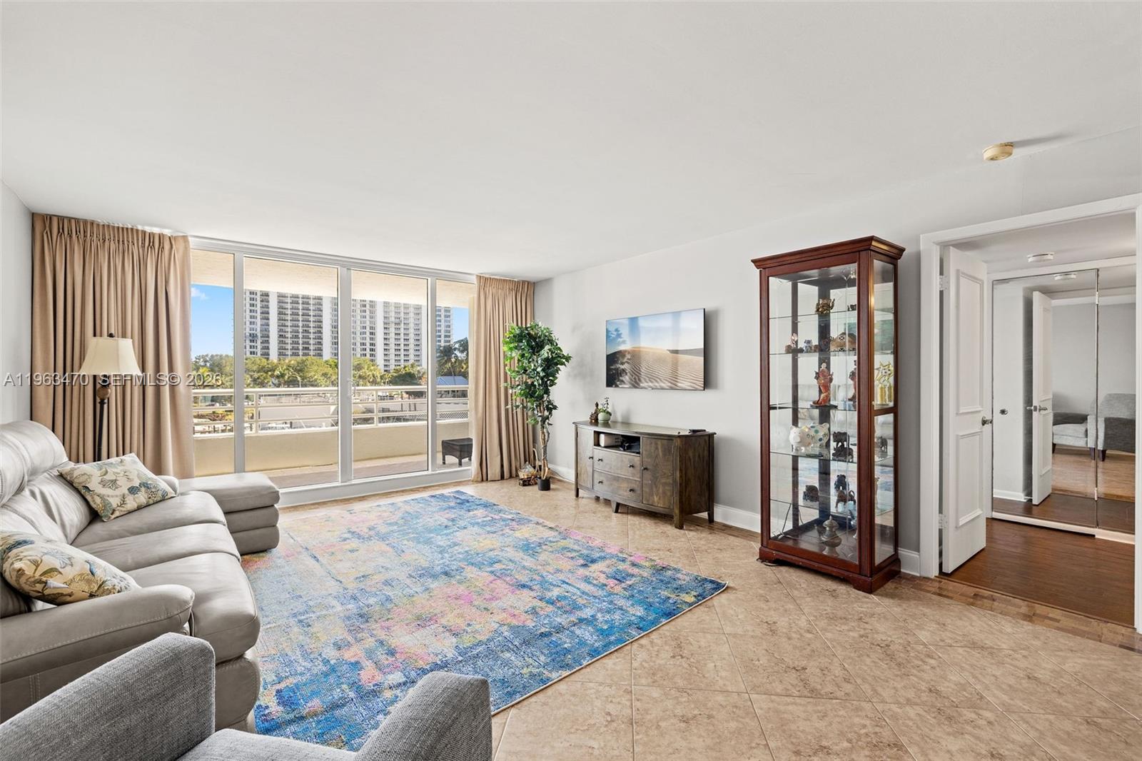A living room features tile floors, a large area rug, a display cabinet, and balcony access — 4201 N Ocean Blvd # 208, Boca Raton FL 33431, BOCA RATON, FL