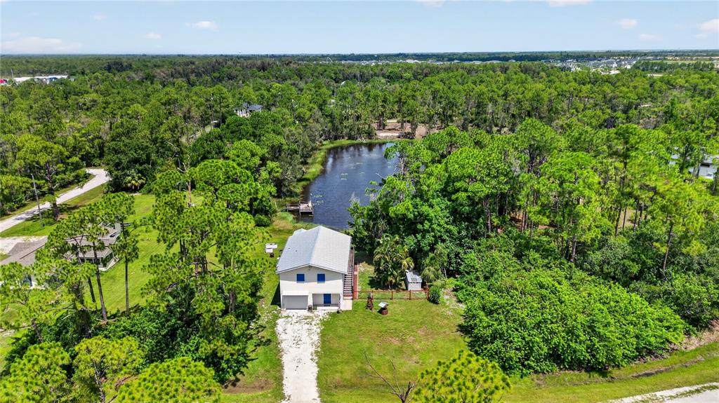An aerial view shows a two-story house with a metal roof beside a pond — 12141 BUENOS COURT, PUNTA GORDA, FL