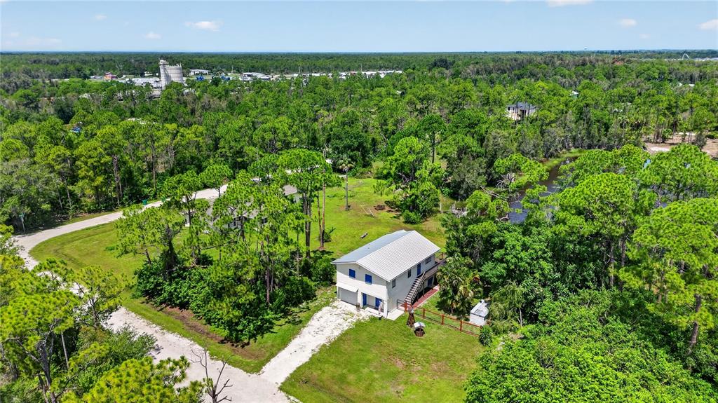 An aerial view shows a two-story house with a metal roof surrounded by dense trees — 12141 BUENOS COURT, PUNTA GORDA, FL