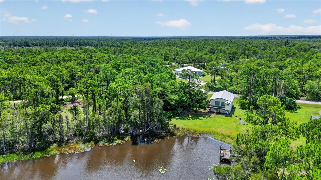 An aerial view shows a house with a dock on a pond surrounded by trees — 12141 BUENOS COURT, PUNTA GORDA, FL