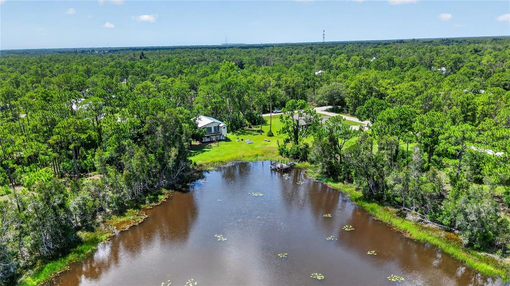An aerial view of a house situated on a grassy lot beside a small pond — 12141 BUENOS COURT, PUNTA GORDA, FL