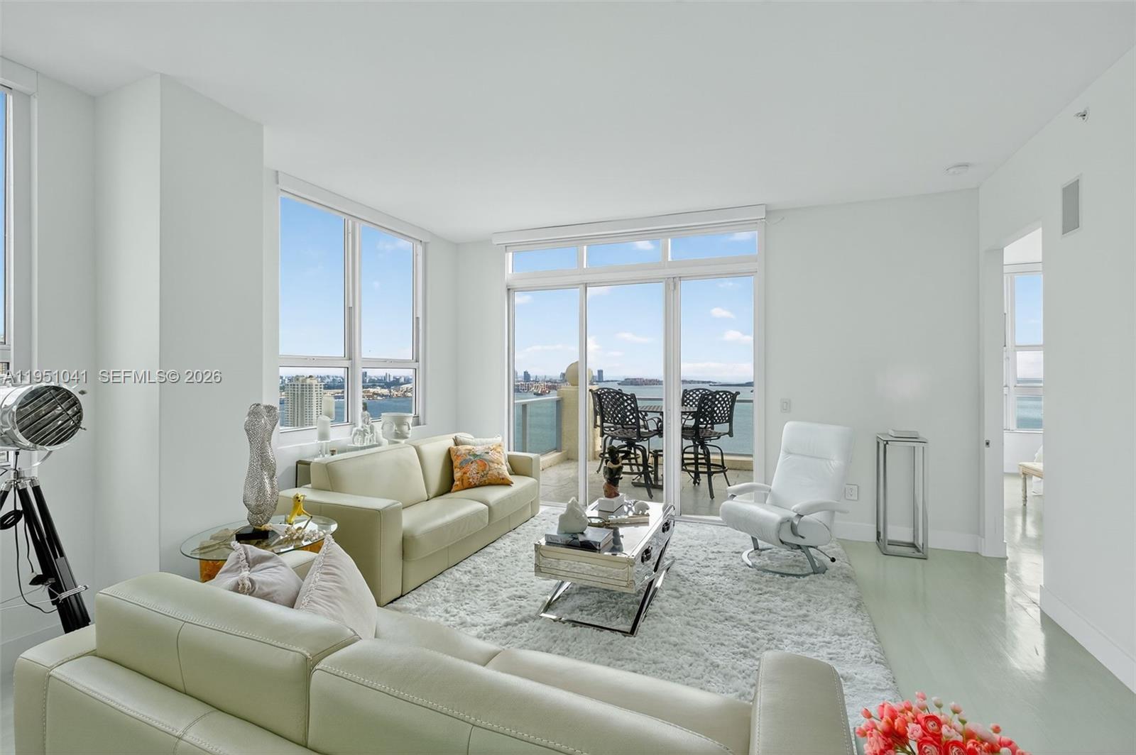 A bright living room features light-colored furniture, a plush rug, and a balcony overlooking water — 1155 Brickell Bay Dr, Miami FL 33131, MIAMI, FL