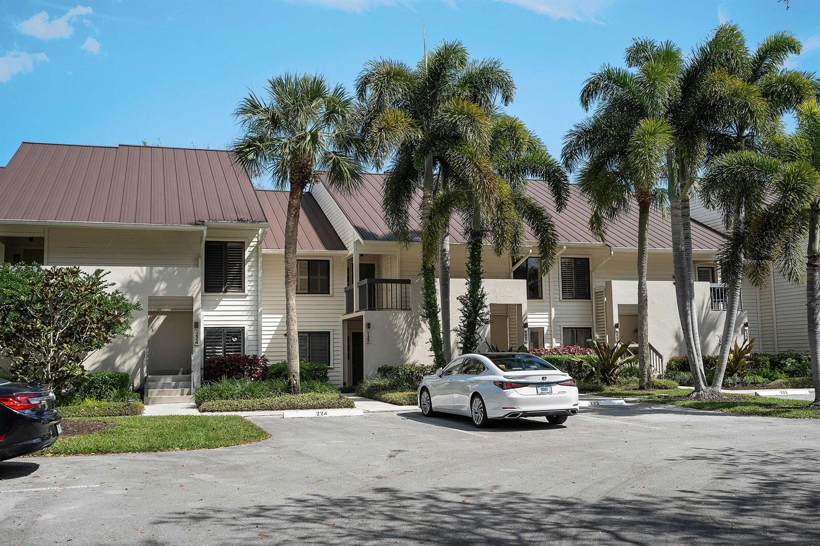 A white sedan is parked in front of a two-story apartment building with palm trees — 6403 SE Brandywine Court # 223, Stuart FL 34997, STUART, FL