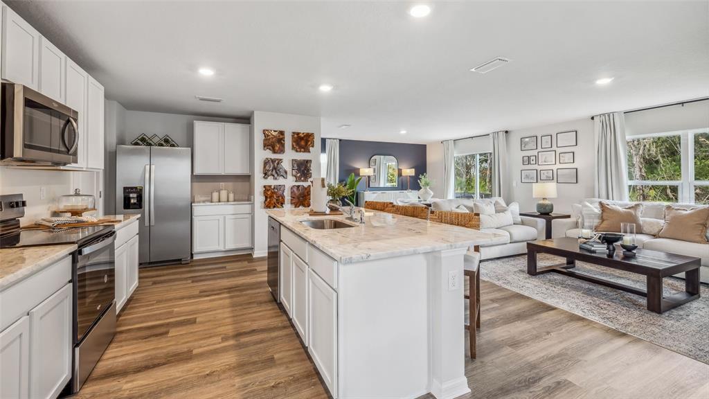 An open-concept kitchen and living area with white cabinets, stainless steel appliances, and wood flooring — 9965 MORNING MEADOWLARK TRAIL, PARRISH, FL