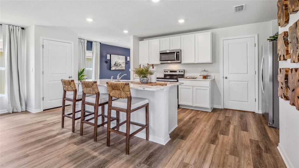A modern kitchen features white cabinetry, a central island with green stools, and light flooring — 9965 MORNING MEADOWLARK TRAIL, PARRISH, FL