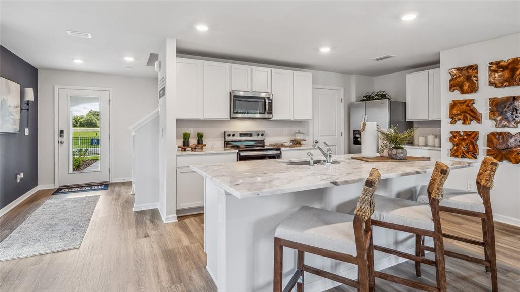 A kitchen features white cabinets, a central island with green chairs, and light wood flooring — 9965 MORNING MEADOWLARK TRAIL, PARRISH, FL