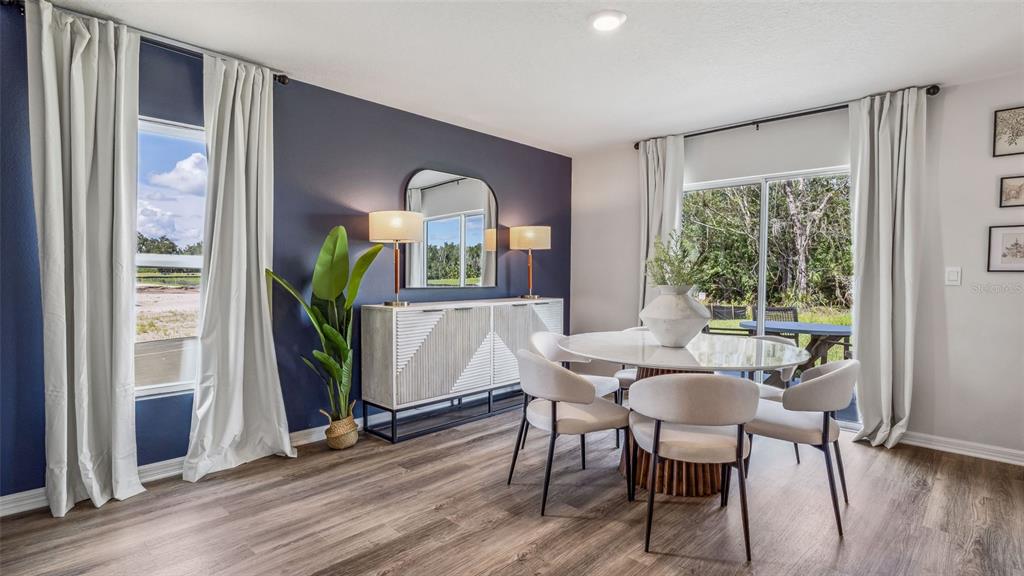 An open-concept dining and living area features wood-look flooring, a wooden dining table, and sliding doors — 9965 MORNING MEADOWLARK TRAIL, PARRISH, FL