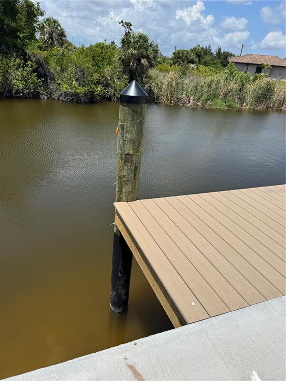 A wooden dock extends over a canal toward a grassy bank with trees and a house — 13156 AMARYLLIS CIRCLE, PORT CHARLOTTE, FL