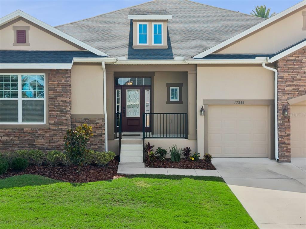 A single-story house exterior features a stone facade, a covered entryway, and a garage — 17286 HICKORY WIND DRIVE, CLERMONT, FL