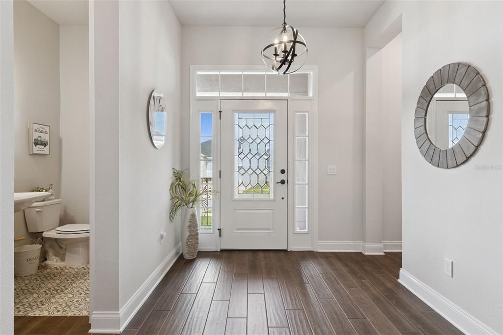 An entryway features dark wood flooring, a decorative front door, and an adjacent powder room — 17286 HICKORY WIND DRIVE, CLERMONT, FL