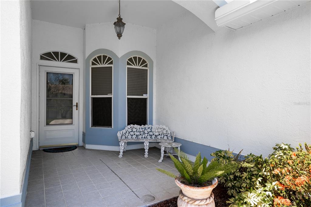 A covered entryway features a white door, two windows, a metal bench, and potted plants — 13109 DOBREE PLACE UNIT 29, RIVERVIEW, FL