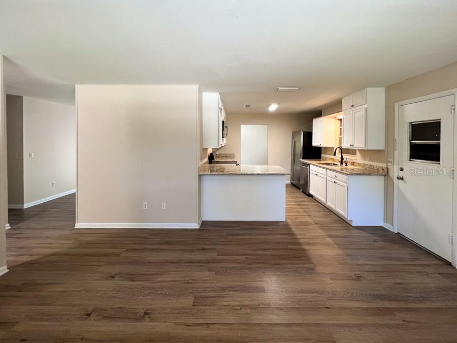 A kitchen with white cabinets and a peninsula opens to a living area with wood-look flooring — 2110 NW 54TH TERRACE, GAINESVILLE, FL